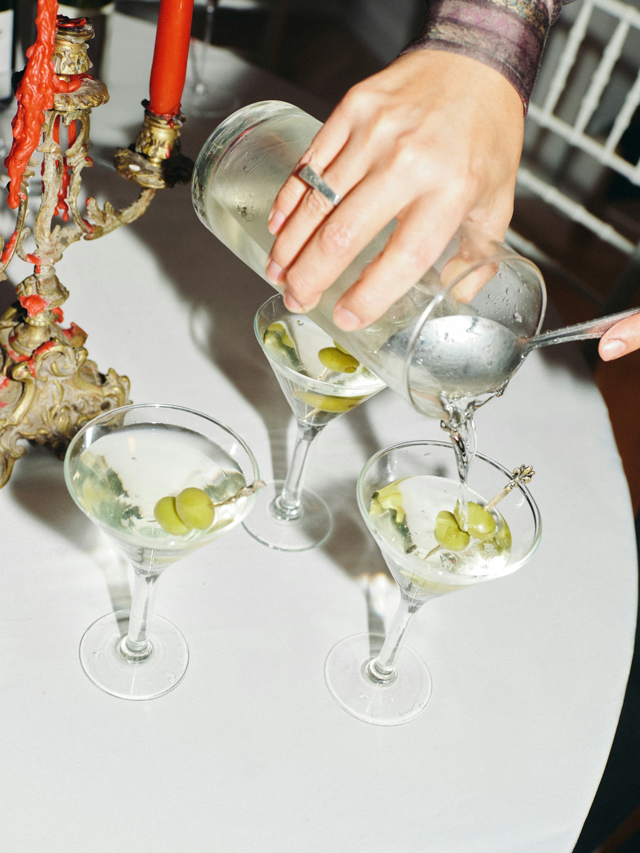Close up of a person pouring a martini into a martini glass. Two full martini glasses are placed on the table next to it.